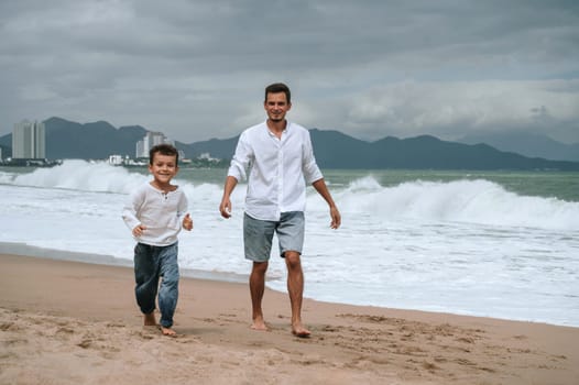 happy dad with a child son are walking along the beach by the sea on a summer vacation