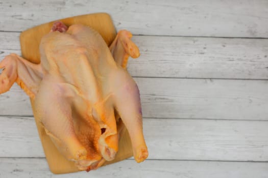 Close-up top view of a butchered raw chicken lying on a wooden cutting board against a white wood background with space for text. The concept of cooking, diet menu, ingredients. High quality photo