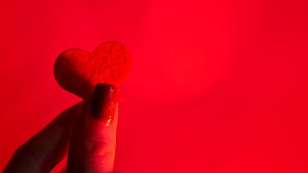 Woman Hands Attach a Decorative Red Heart of love Against a Neon Background for International Valentine's Day, February 14