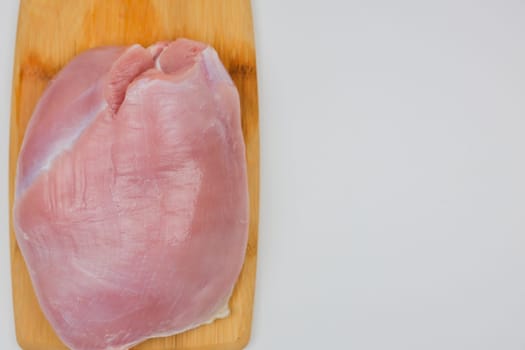 On a wooden cutting board lies a close-up piece of turkey meat on a white background with space for text. The concept of a diet menu, cooking. High quality photo