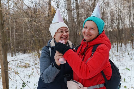 Two friends embrace the winter chill while hiking through a snowy forest, laughing and capturing the spirit of friendship