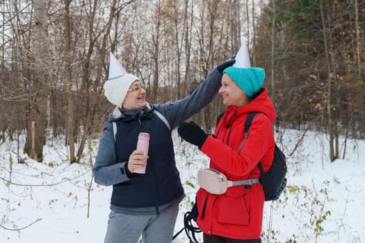 Two friends embrace the winter chill while hiking through a snowy forest, laughing and capturing the spirit of friendship