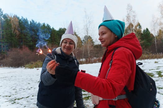 Celebrating joyfully in a snowy forest with sparklers and festive hats during a chilly winter gathering