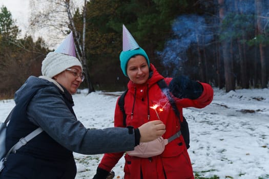 Two cheerful individuals share a playful moment in a snowy landscape, wearing festive hats while holding sparklers.