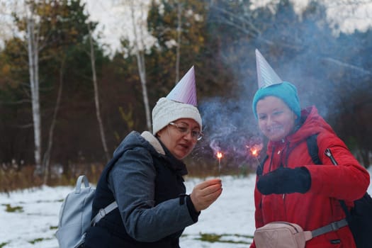 Two cheerful individuals share a playful moment in a snowy landscape, wearing festive hats while holding sparklers.