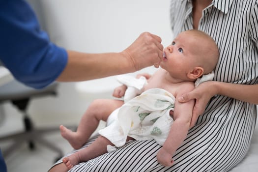 Pediatrician administring oral vaccination against rotavirus infection to little baby in presence of his mother. Children health care and disease prevention.