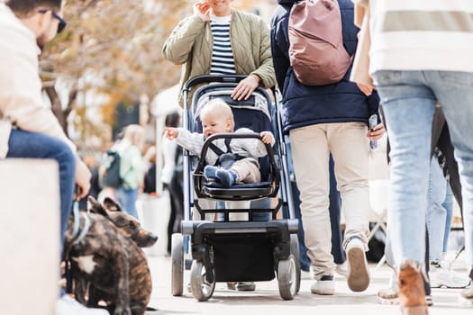 Mother walking and pushing his infant baby boy child in stroller in crowd of people wisiting sunday flea market in Malaga, Spain