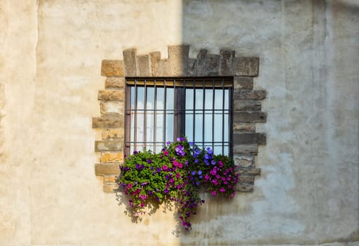 Wall with window and flowers in the shadow half. Bergamo. Italy.