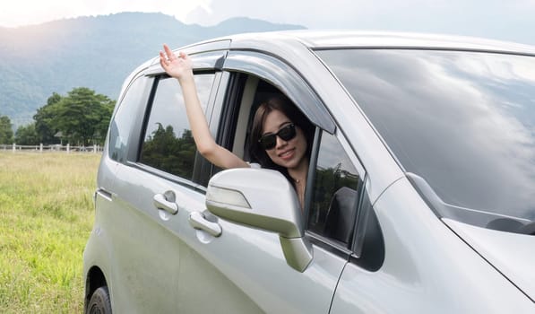 Happy young Asian woman enjoying a road trip and having fun waving at the air outside the car..