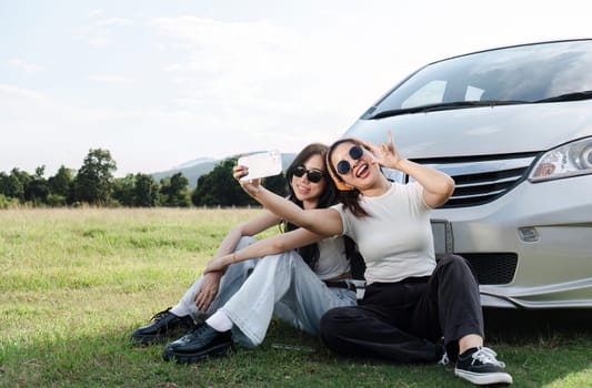 Two young women in white t-shirts and jeans sit back and relax, taking selfies together with their cell phones..