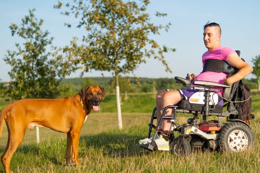 A happy young man with a disability in a wheelchair is accompanied by his service dog.