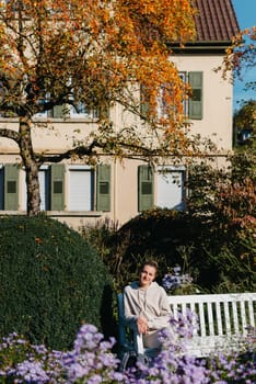 a girl sits on a bench in the park and enjoys the sun. Portrait young adult attractive woman enjoy sitting on bench and relaxing calm carefree rest in city park against green grass and trees on sunny day. Single female person relaxing chilling outdoors