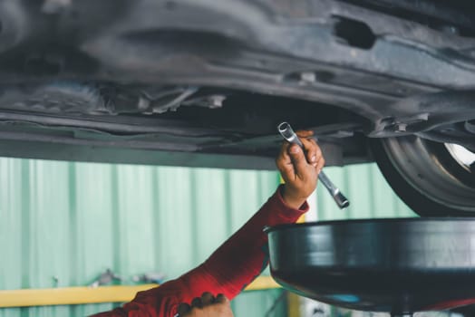 Car mechanic drain the old lubricant engine oil at car garage for changing the oil in a car engine