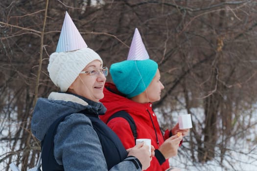 Two friends savoring warm beverages while chatting in a snowy forest.