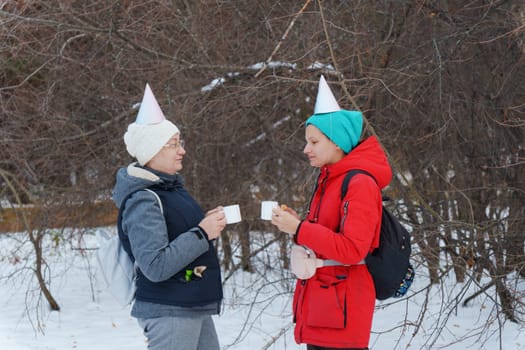 Two friends savoring warm beverages while chatting in a snowy forest.