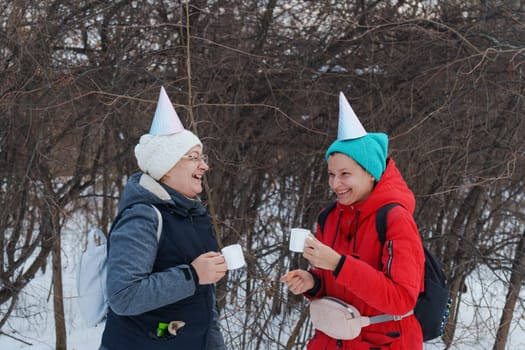 Two friends enjoying winter treats in the snowy forest, celebrating with festive party hats