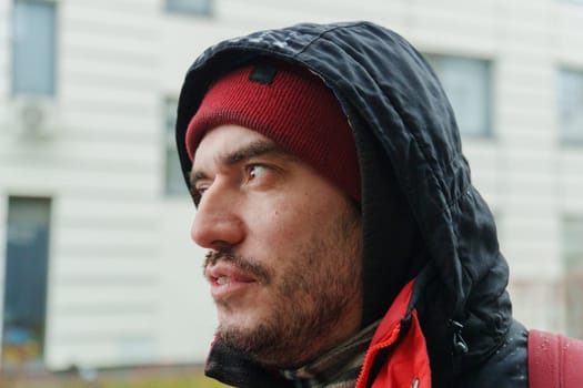 Sporting a red beanie and warm jacket, a man gazes thoughtfully at the viewer, reflecting resilience and sincerity