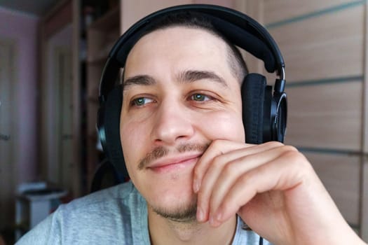 Smiling young man wearing headphones enjoys casual moment at home while engaging in online chat or gaming
