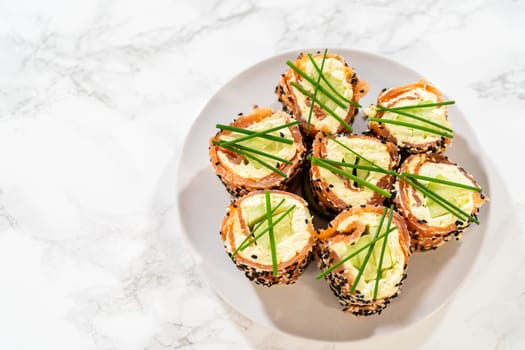 A beautiful arrangement of smoked salmon jumbo cream cheese rolls served on a plate. The rolls are evenly garnished with fresh chives and feature a crunchy sesame seed coating. This dish is a perfect centerpiece for festive parties and elegant gatherings.
