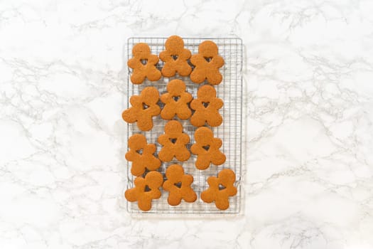Flat lay close-up showing neatly arranged gingerbread man cookies cooling on a wire rack, showcasing their golden-brown tones and festive shapes.