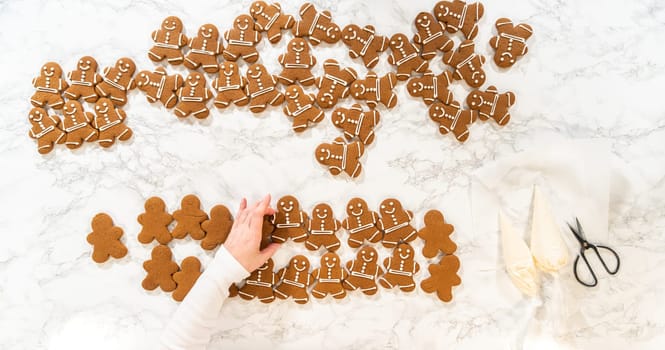 A festive arrangement of decorated gingerbread man cookies spread across a marble countertop, surrounded by holiday-themed baking tools, creating a cheerful and seasonal vibe.
