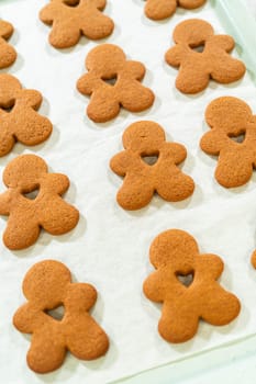 Angled view of baked gingerbread men cookies with heart-shaped cutouts on a parchment-lined baking sheet.