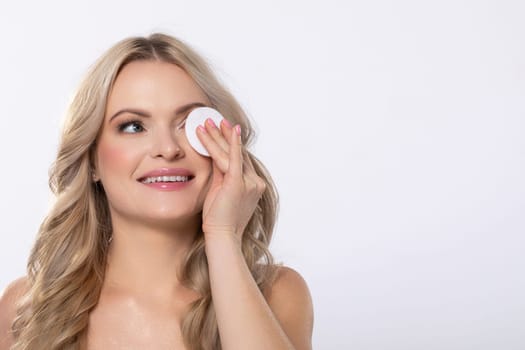 A joyful woman with a delightful smile is applying skincare with a cotton pad, emphasizing beauty and selfcare