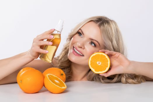 A radiant woman showcases orange skincare products and fresh oranges, highlighting wellness and natural beauty