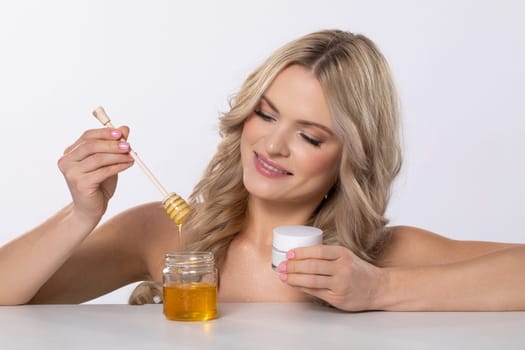A joyful woman happily indulging in her skincare routine while using honey and a luxurious cream product