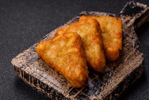 Hash browns with potatoes and onions, salt and spices on a dark concrete background
