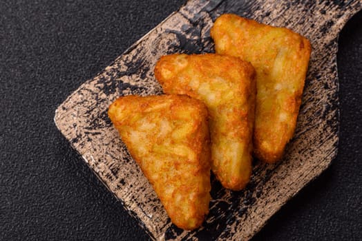 Hash browns with potatoes and onions, salt and spices on a dark concrete background