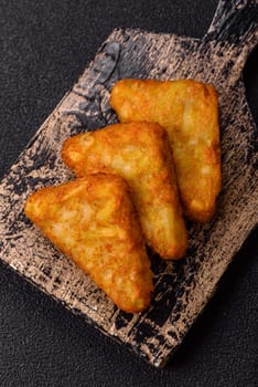 Hash browns with potatoes and onions, salt and spices on a dark concrete background