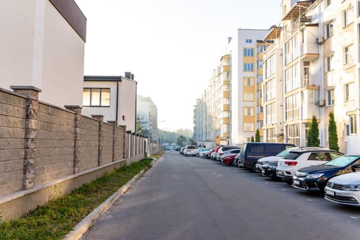 A calm morning displays a residential street lined with various parked cars. The sunlight filters through nearby buildings, highlighting the tranquil atmosphere of the neighborhood. Ukraine, Vinnytsia, 2021.01.15