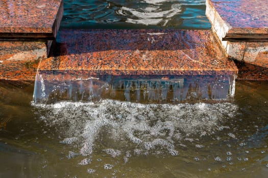 Water flows gently over a smooth granite ledge, creating bubbles and ripples in a tranquil outdoor environment bathed in natural light. This peaceful moment captures the beauty of natures movement.