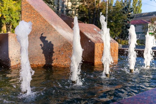 Gentle water jets erupt from stone structures, creating a lively atmosphere in a bustling city park. Visitors enjoy the refreshing sounds and sights on a clear afternoon.