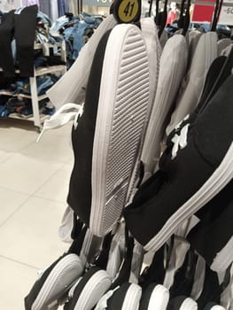 A pair of black shoes with white soles hangs prominently on a rack inside a retail store. Various clothing items are visible in the background, creating a busy shopping atmosphere.