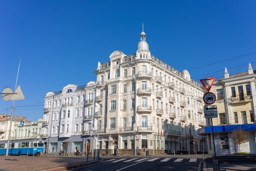 An elegant historic building stands in the city center under a clear blue sky. Street signs and a tram line create a lively urban atmosphere on a bright day. Ukraine, Vinnytsia, 2021.01.15