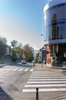 A modern building stands prominently beside a peaceful street. Clear blue skies above enhance the tranquil atmosphere while trees along the road create a pleasing ambiance. Ukraine, Vinnytsia, 2021.01.15