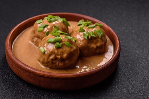 Meatballs with salt and spices in creamy caramel sauce on a dark concrete background