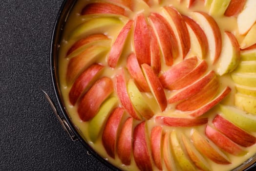 Raw sweet apple pie in a mold prepared for baking on a dark concrete background