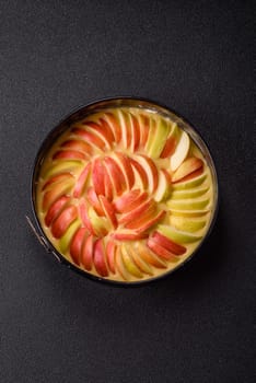Raw sweet apple pie in a mold prepared for baking on a dark concrete background