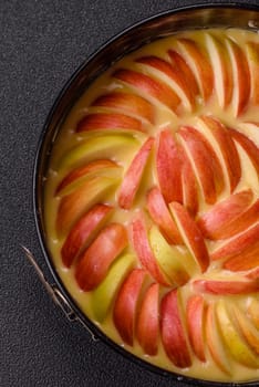 Raw sweet apple pie in a mold prepared for baking on a dark concrete background