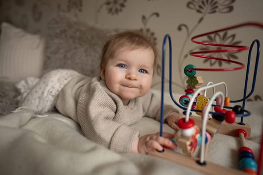 Adorable 6-month baby playing with educational toy on bed coat. Activity for motor and sensory development. High quality photo