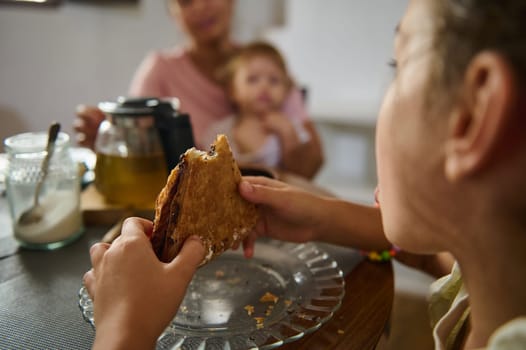 A child savoring a pastry while dining with family during breakfast in a warm home, featuring a relaxed and intimate atmosphere in a cozy kitchen environment.