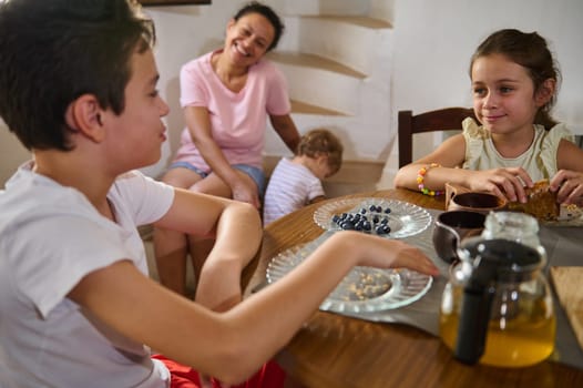 A family gathers around a wooden table for breakfast, sharing blueberries and tea together. The atmosphere is warm, depicting a close and joyful moment of togetherness and family time during a peaceful morning.