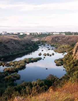 A huge wide river flows between steep banks. A city is visible on the horizon. Autumn forest on the banks of the river. Cliffs of granite stones, Bushes grow in the middle of the river. southern bug