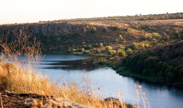 a huge wide river flows among steep banks. autumn forest on the banks of the river. cliffs of granite stones. calm blue water surface. southern bug, ukraine