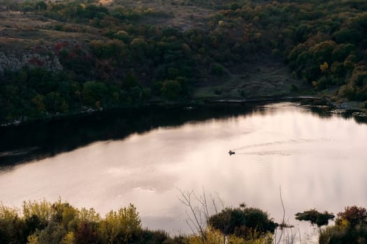 a huge wide river flows among steep banks on the water surface a small boat. autumn forest on the banks of the river. cliffs of granite stones. calm water surface on the river. southern bug, ukraine