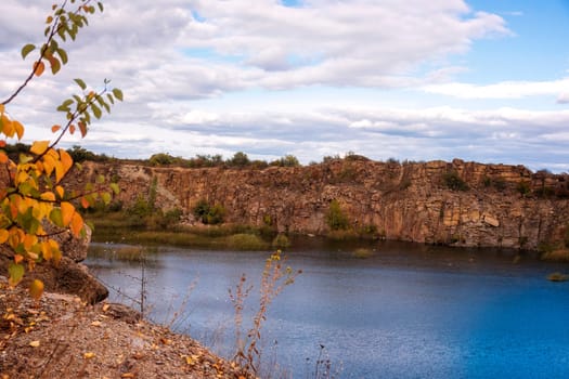 fantastic autumn in a mountain canyon. huge granite boulders around a huge bright blue lake. aktovsky canyon in ukraine with cliffs. trees with yellow leaves grow on the tops.