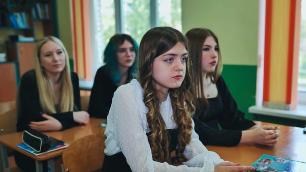 Four teenage girls are seated at desks in a classroom, engaged in a lecture and actively participating in the school day